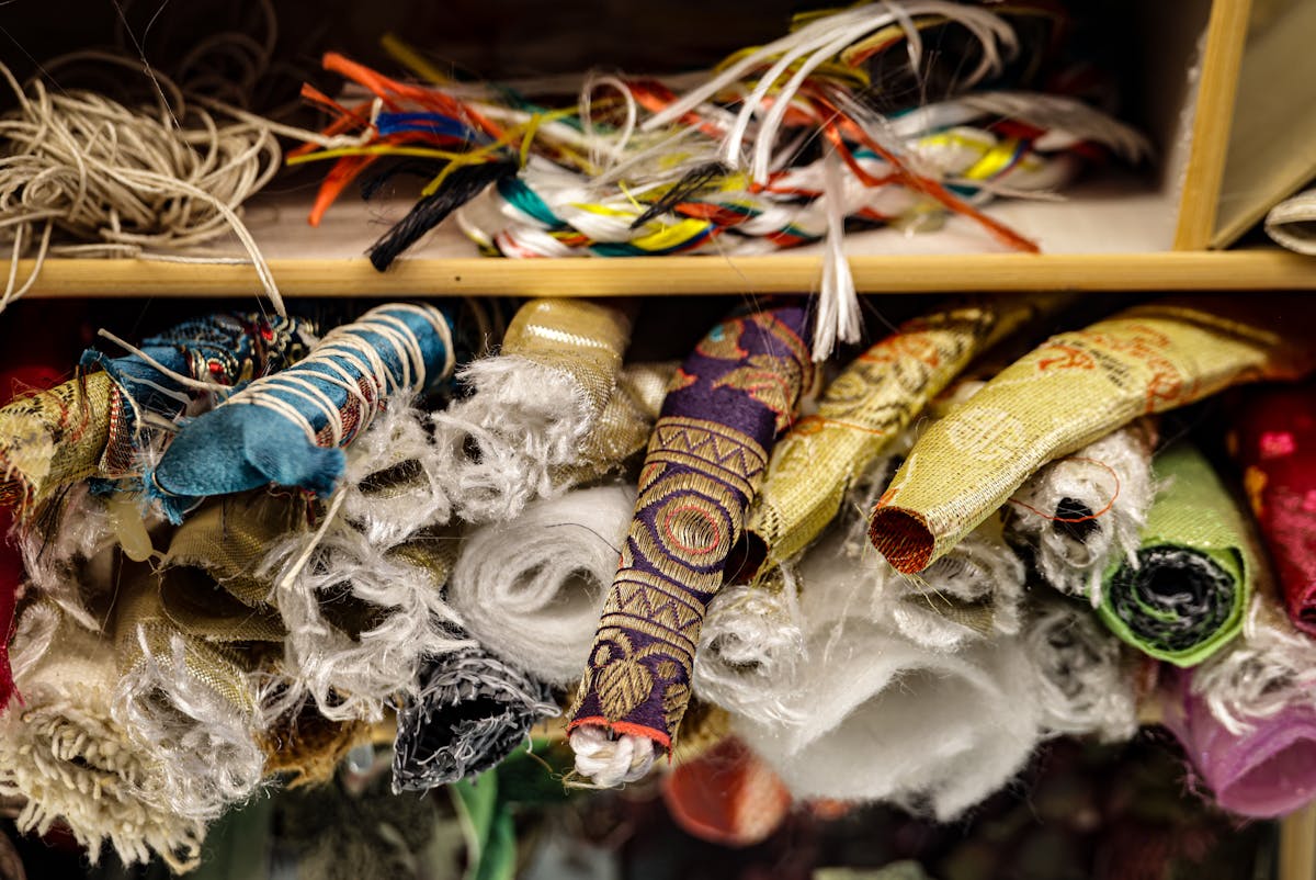 Close-up of mixed artisan fabrics and threads stored on a shelf.