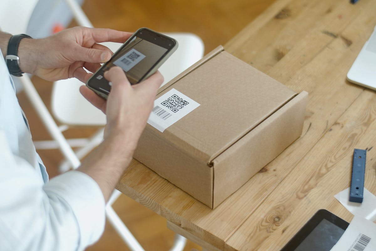 Hands using a phone to scan a QR label on a plain cardboard package.